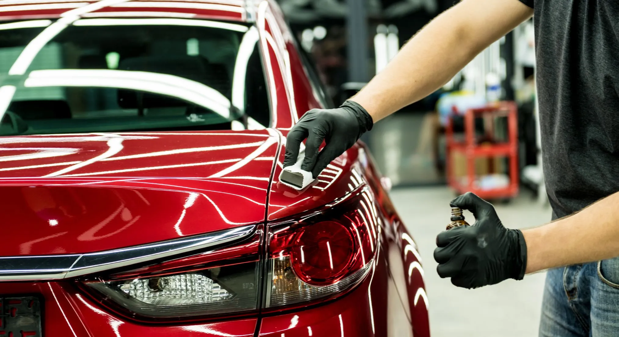 Ceramic coating being applied to the glossy red paint of a car by a professional installer wearing black gloves
